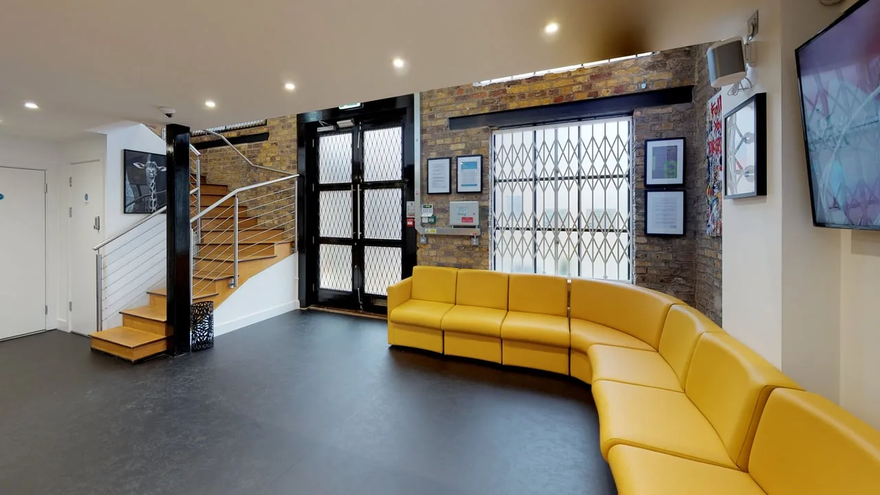 Reception at our Brentford practice — exposed brick, a curved yellow sofa and a timber staircase